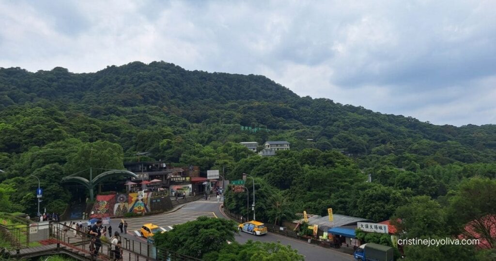 A scenic view of lush green hillsides and local shops along a winding road in Maokong.