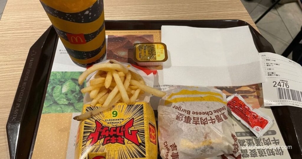 A McDonald's tray with a double cheeseburger, spicy chicken nuggets, fries, and a drink on a wooden table.