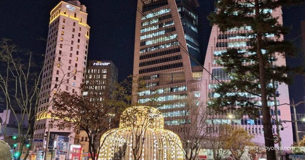 Illuminated golden light dome sits in front of the modern Post Tower building at night in Myeongdong.