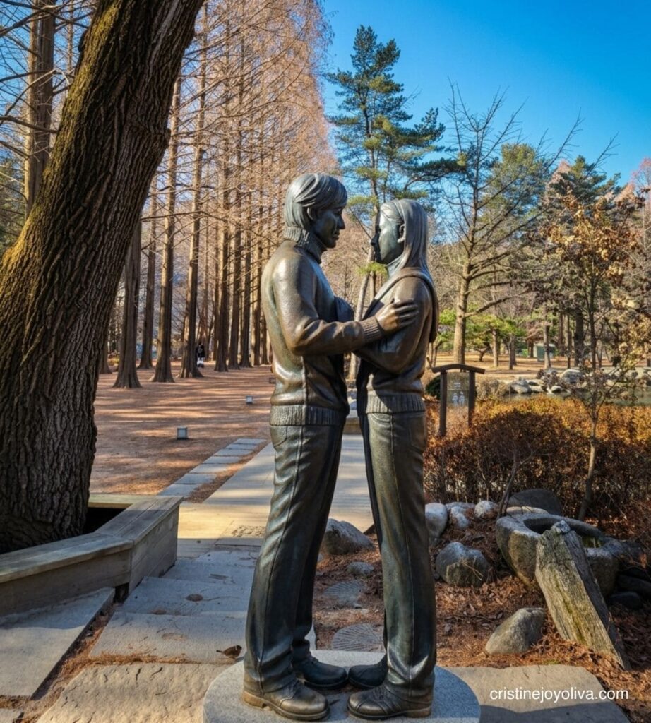 Bronze statue of a couple embracing along a tree-lined pathway on Nami Island