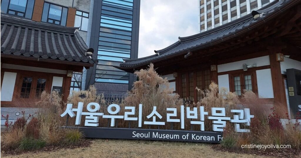 Traditional hanok-style exterior of the Seoul Museum of Korean Folk Music with modern city buildings in the background.
