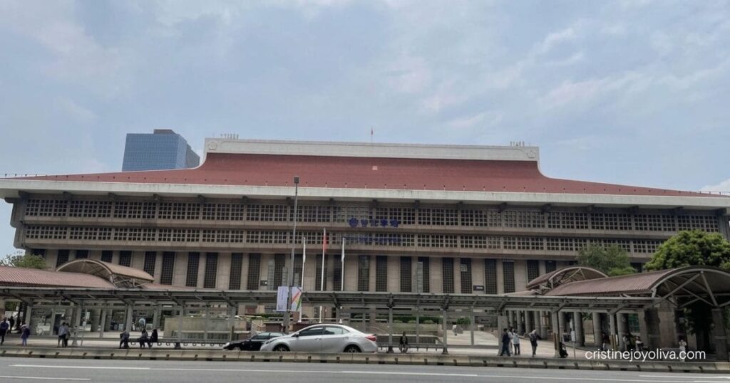 The wide facade of the Taipei Main Station building with red tiled roofs under a cloudy sky.