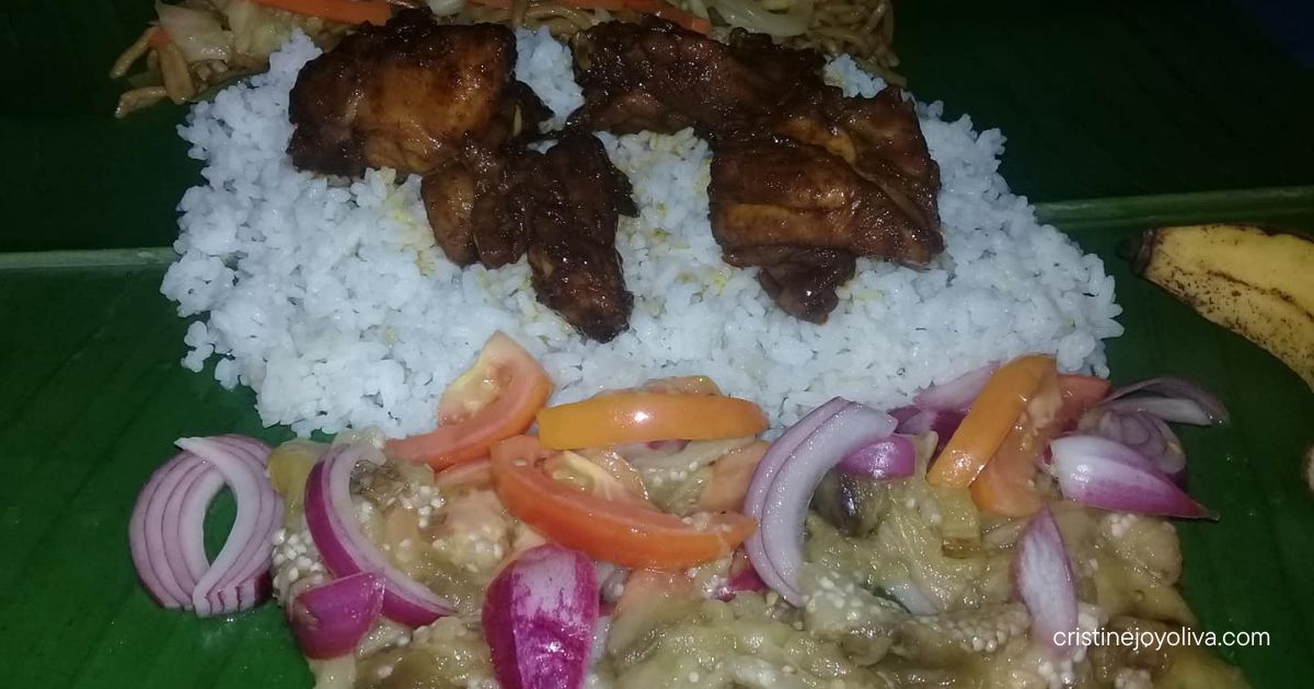 Filipino boodle fight meal on a banana leaf featuring adobo chicken, rice, and fresh ensaladang talong in Antique, Philippines