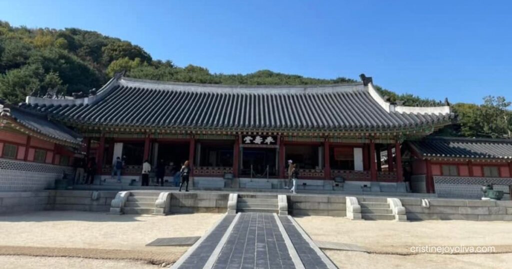 Bongsudang, the main hall of Hwaseong Haenggung Palace, with a gray tiled roof, red pillars, and visitors under a blue sky