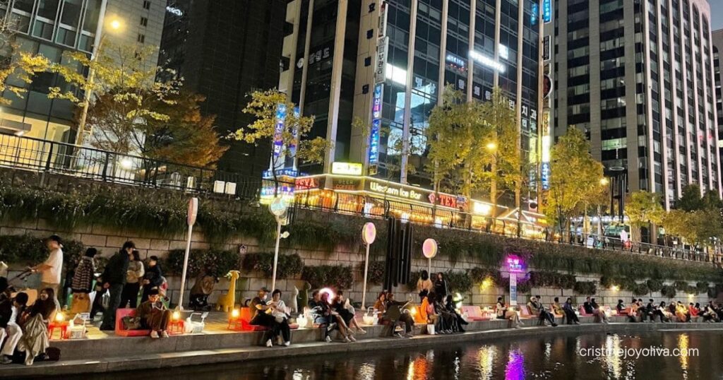 People relaxing along Cheonggyecheon stream at night, with city lights reflected in the water