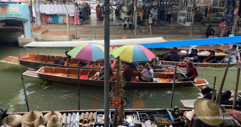 Tourist boats under colorful umbrellas on the canal at Damnoen Saduak Floating Market, with straw hats in the foreground