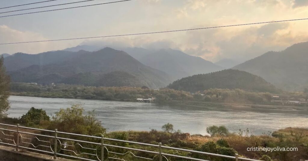 Scenic river and mountain view from railway tracks in Gapyeong, South Korea, with sunlight filtering through clouds.