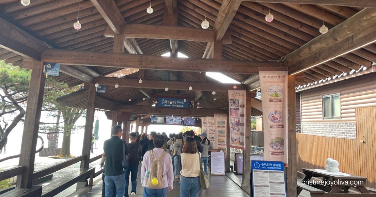 Visitors walking through a wooden pavilion decorated with hanging lights and banners on Nami Island