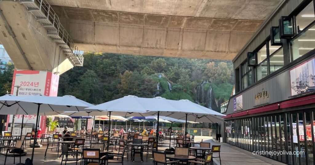Empty outdoor seating at Pokpo Cafe in Seoul with a waterfall in the background on a quiet morning