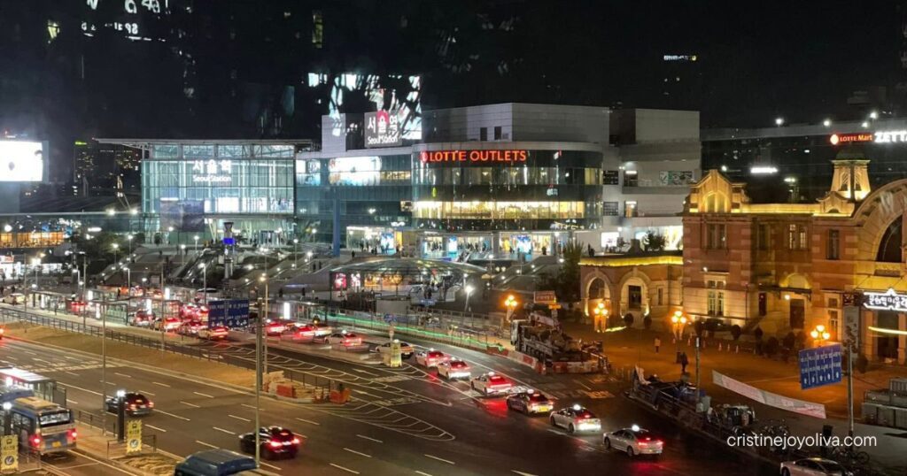 Seoul Station and Lotte Outlets lit up at night, with taxis and buses on the road and the old station building at right
