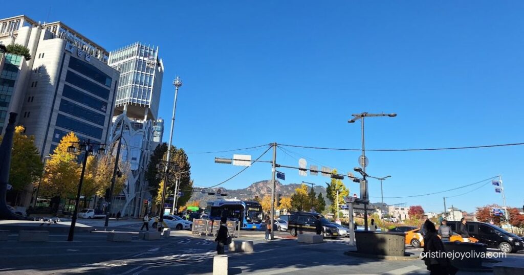 Sunny Seoul street in November with yellow autumn trees, a blue city bus, and a mountain in the distance
