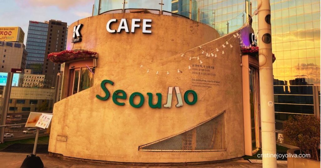 Round concrete café with a green Seoullo sign and string lights on the Seoullo 7017 walkway at dusk
