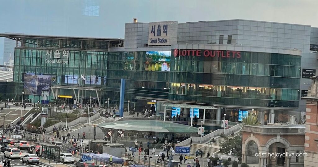 Modern Seoul Station glass building with Lotte Outlets and crowds on the plaza, seen from above on a cloudy day